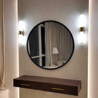 Round mirror with a dark frame on a wall with two wall lights and a wooden console below.