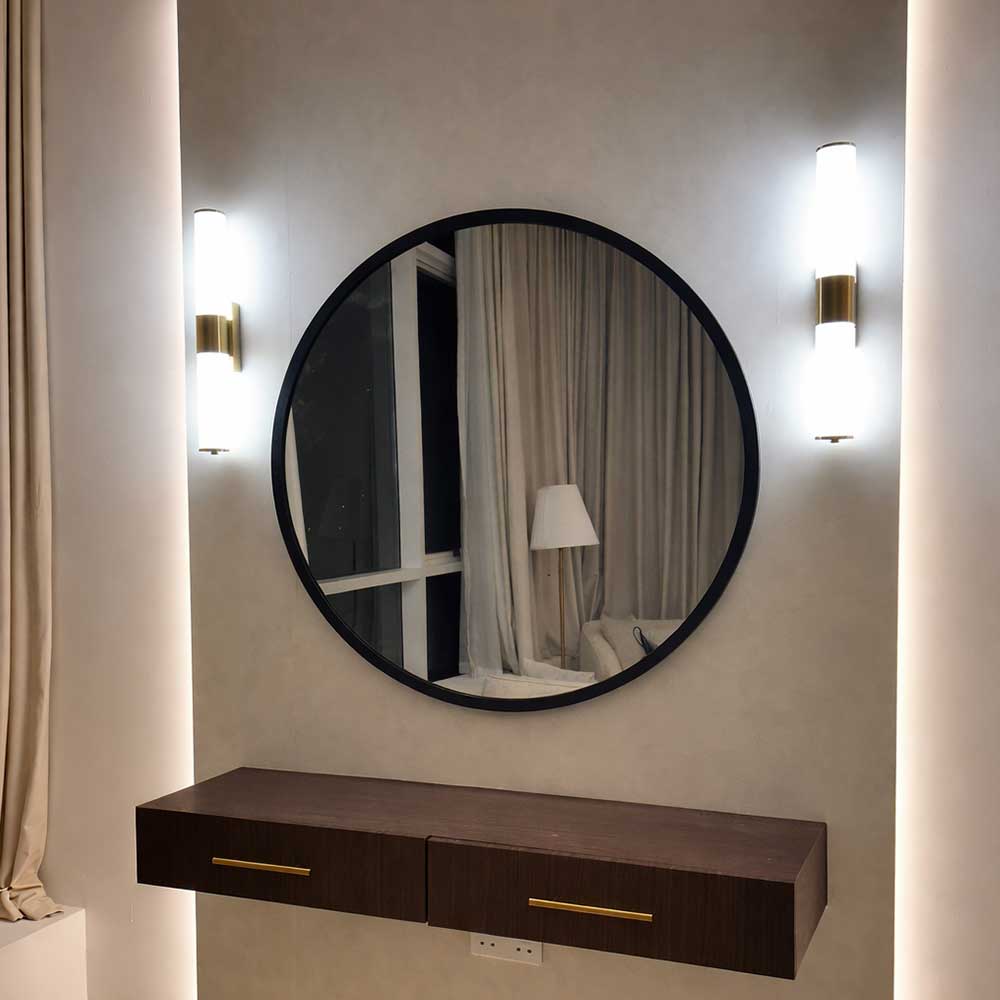 Round mirror with a dark frame on a wall with two wall lights and a wooden console below.