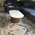 Coffee table with marble top and wooden base in front of a dark gray sectional sofa on a patterned rug.